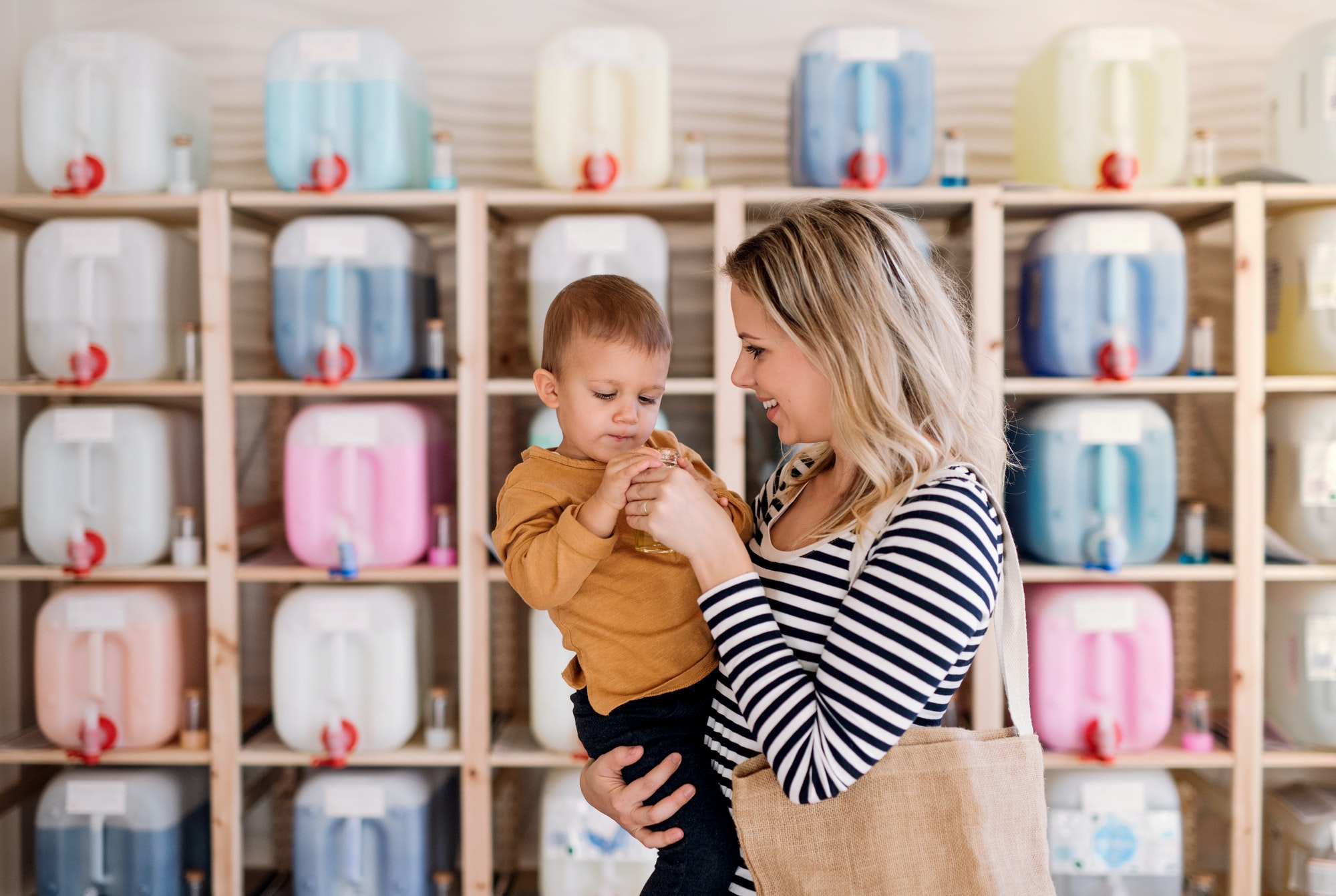 A young woman with a toddler boy buying liquids in zero waste shop.